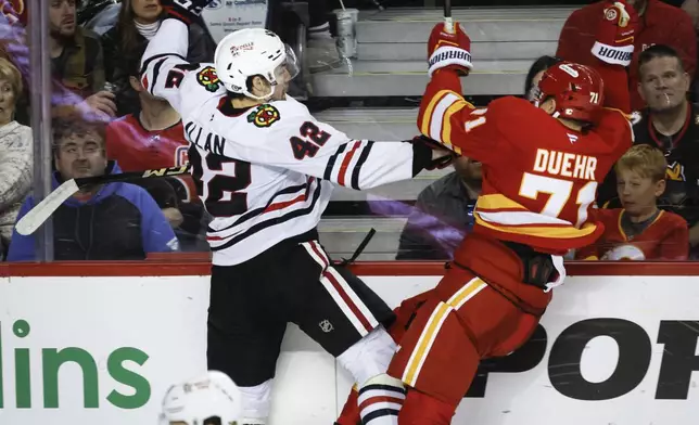 Chicago Blackhawks' Nolan Allan, left, checks Calgary Flames' Walker Duehr during the third period of an NHL hockey game in Calgary, Alberta, on Saturday, Dec. 21, 2024. (Jeff McIntosh/The Canadian Press via AP)