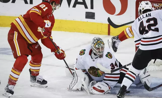 Chicago Blackhawks goalie Petr Mrazek, center, tries to grab the puck as Calgary Flames' Kevin Rooney (21) digs for it during the second period of an NHL hockey game in Calgary, Alberta, Saturday, Dec. 21, 2024. (Jeff McIntosh/The Canadian Press via AP)