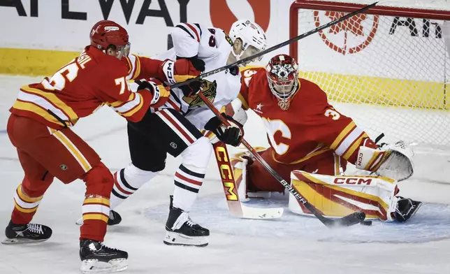 Chicago Blackhawks' Ilya Mikheyev, center, tries to get the puck past Calgary Flames goalie Dustin Wolf, right, as Martin Pospisil checks during the first period of an NHL hockey game in Calgary, Alberta, Saturday, Dec. 21, 2024. (Jeff McIntosh/The Canadian Press via AP)Hockey