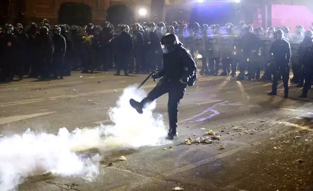 A police officer kicks a canister during a rally against the government's decision to suspend negotiations on joining the European Union for four years, outside the parliament's building in Tbilisi, Georgia, early Monday, Dec. 2, 2024. (AP Photo/Zurab Tsertsvadze)