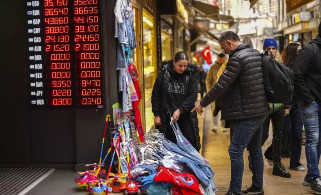 A seller attends to a man, next to a currency exchange shop at Eminonu commercial area, in Istanbul, Turkey, Thursday, Dec. 26, 2024, as Turkey's central bank lowered its key interest rate by 2.5 percentage points to 47.5% carrying out its first rate cut in nearly two years as it tries to control soaring inflation. (AP Photo/Francisco Seco)