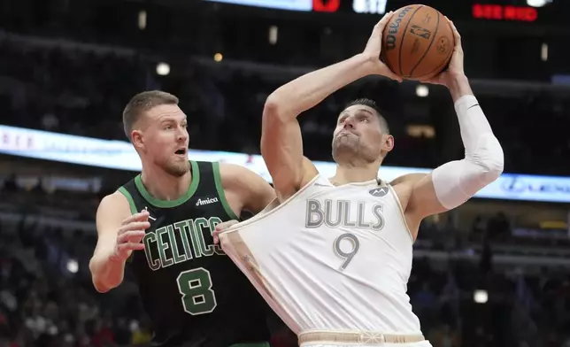 Boston Celtics' Kristaps Porzingis (8) tugs on the jersey of Chicago Bulls' Nikola Vucevic as Vucevic drives to the basket during the second half of an NBA basketball game Saturday, Dec. 21, 2024, in Chicago. (AP Photo/Charles Rex Arbogast)