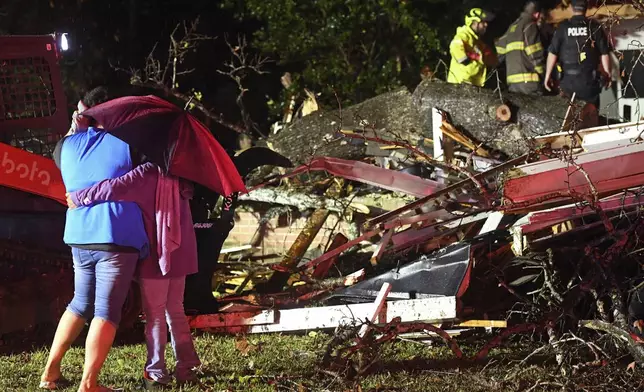 Bystanders hug as first responders work to free a victim after a tree fell on a house in Natchez, Miss., Saturday, Dec. 28, 2024. (Thomas Graning/The Natchez Democrat via AP)