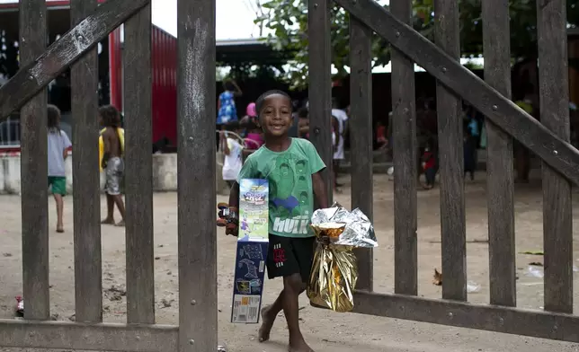 A child carries Christmas donations from the SOMOS social movement, a non-governmental organization working to fight hunger, in the Jardim Gramacho favela, in Duque de Caxias, Rio de Janeiro state, Sunday, Dec. 15, 2024. (AP Photo/Bruna Prado)