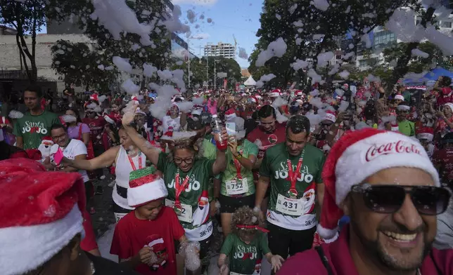 People walk through foam during a Santa Run event in Caracas, Venezuela, Sunday, Dec. 15, 2024. (AP Photo/Ariana Cubillos)