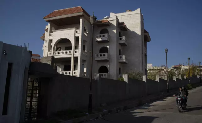 Men ride a motorcycle past a property owned by ousted Syrian President Bashar Assad's family in Qardaha, Syria, on Tuesday, Dec. 17, 2024. (AP Photo/Leo Correa)