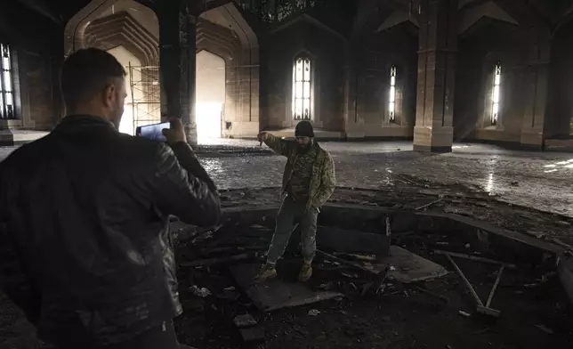 A man records a video of a Syrian fighter standing atop the burned-out tomb of Syria's former President Hafez Assad at his mausoleum in Qardaha, Syria, on Tuesday, Dec. 17, 2024. (AP Photo/Leo Correa)