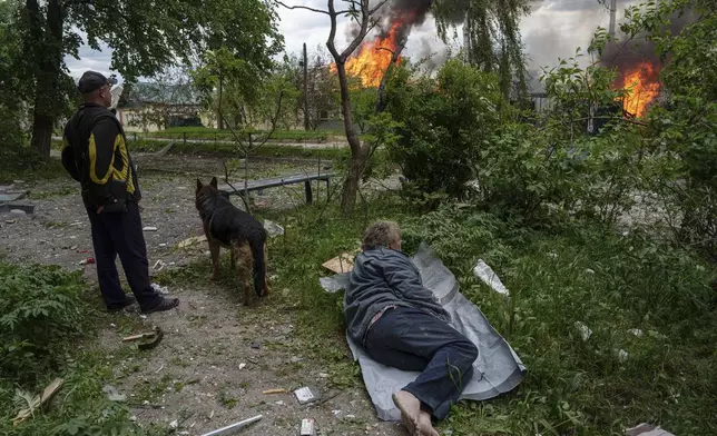 A man lies on the ground as he watches his burning house destroyed by a Russian airstrike in Vovchansk, Ukraine, on Saturday, May 11, 2024. (AP Photo/Evgeniy Maloletka)