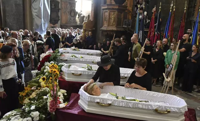 People mourn near the coffins of Yaroslav Bazylevych's family members during the funeral service in the Garrison Church in Lviv, Ukraine, Friday, Sept. 6, 2024. (AP Photo/Mykola Tys)