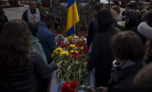 People bid farewell and lay flowers in the coffin of fallen Ukrainian serviceman Vadym Popelniuk, born in 1991, during a religious service in Independence Square in Kyiv, Ukraine, Friday, April 5, 2024. (AP Photo/Vadim Ghirda)