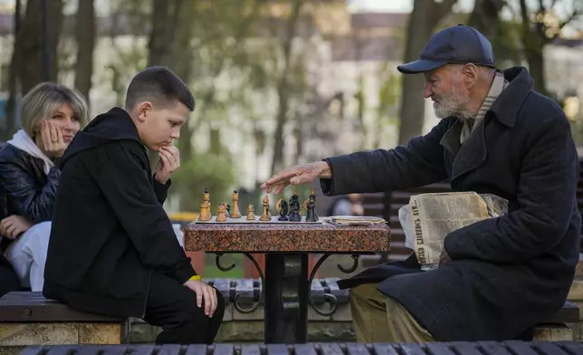 An elderly man plays chess with a boy training him to perfect his game in Taras Shevchenko Park, in Kyiv Ukraine, Sunday, April 7, 2024. (AP Photo/Vadim Ghirda)