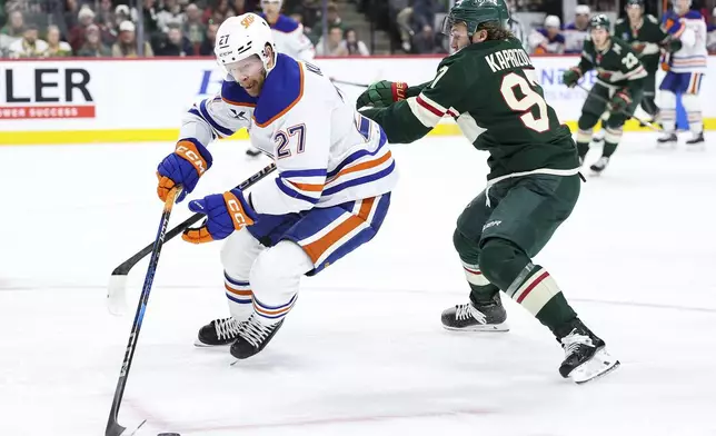 Edmonton Oilers defenseman Brett Kulak, left, skates with the puck as Minnesota Wild left wing Kirill Kaprizov, right, defends during the first period of an NHL hockey game Thursday, Dec. 12, 2024, in St. Paul, Minn. (AP Photo/Matt Krohn)