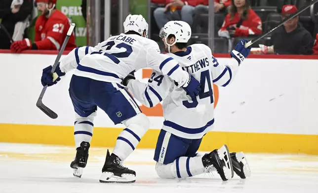 Toronto Maple Leafs center Auston Matthews (34) gets pushed toward the Maple Leafs bench by defenseman Jake McCabe (22) after Matthews lost the blade on his right skate against the Detroit Red Wings during the second period of an NHL hockey game, Saturday, Dec. 14, 2024 in Detroit. (AP Photo/Lon Horwedel)