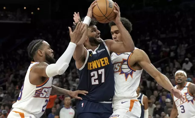 Denver Nuggets guard Jamal Murray drives between Phoenix Suns guard Monte Morris and center Oso Ighodaro during the first half of an NBA basketball game, Wednesday, Dec. 25, 2024, in Phoenix. (AP Photo/Rick Scuteri)