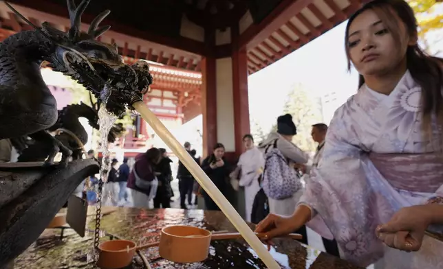 A visitor from Australia cleans her hand with water from a dragon-shaped fountain as part of a ritual to cleanse herself before heading to the main hall of Sensoji Buddhist temple on New Year's Eve in Tokyo, Tuesday, Dec. 31, 2024. (AP Photo/Hiro Komae)