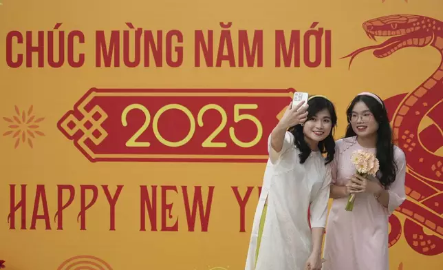 Young women in Vietnamese traditional costumes take a selfie near a New Year countdown concert in Ho Chi Minh city, Vietnam on Tuesday, Dec.31, 2024. (AP Photo/Hau Dinh)