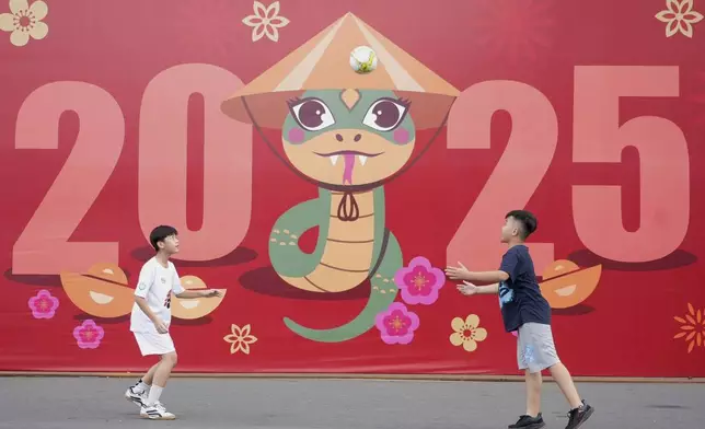 Two boys play football in front of a billboard welcoming the New Year 2025 in Ho Chi Minh city, Vietnam on Tuesday, Dec.31, 2024. (AP Photo/Hau Dinh)