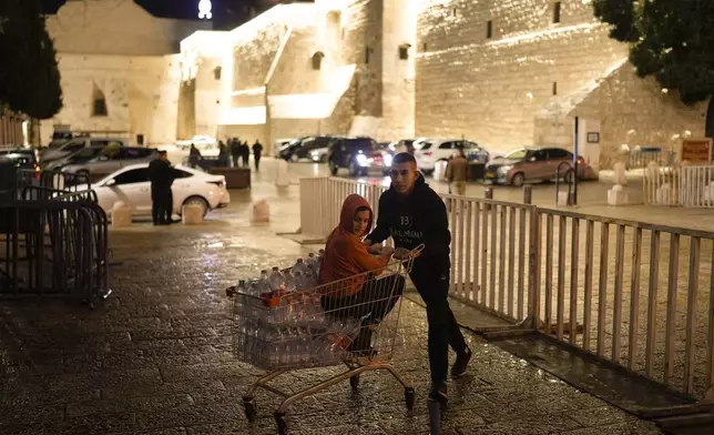 A man carries a supermarket cart next to Church of the Nativity, where Christians believe Jesus Christ was born, ahead of Christmas in the West Bank city of Bethlehem, Monday, Dec. 23, 2024. (AP Photo/Matias Delacroix)