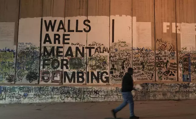 A man walks past the Israel's controversial separation barrier with a mural that reads "Walls are meant for bombing", ahead of Christmas in the West Bank city of Bethlehem, Monday, Dec. 23, 2024. (AP Photo/Matias Delacroix)