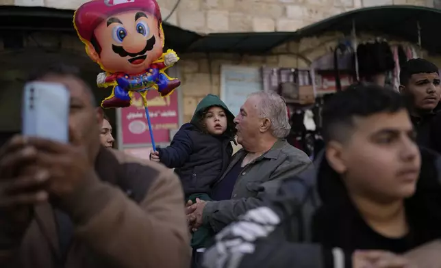 A man holds his granddaughter during the traditional Christian procession towards the Church of the Nativity, traditionally believed to be the birthplace of Jesus, on Christmas Eve, in the West Bank city of Bethlehem, Tuesday, Dec. 24, 2024. (AP Photo/Matias Delacroix)