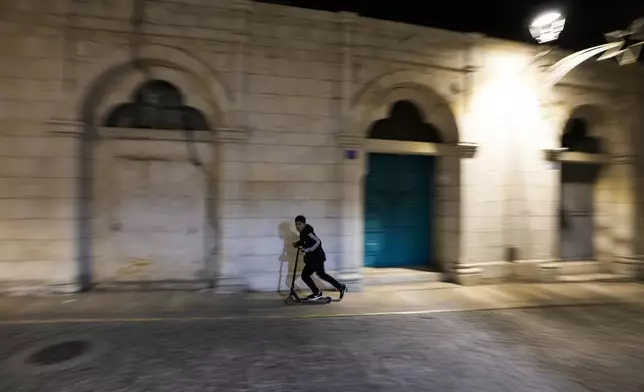 A boy rides his scooter through an alley, ahead of Christmas in the West Bank city of Bethlehem, Monday, Dec. 23, 2024. (AP Photo/Matias Delacroix)