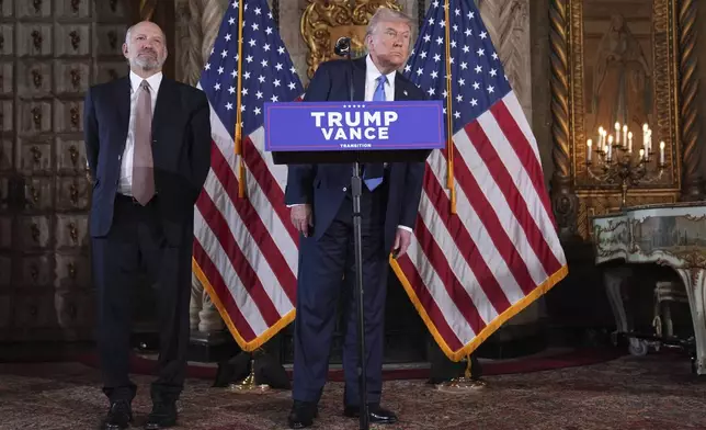 President-elect Donald Trump speaks at a news conference at Mar-a-Lago, Monday, Dec. 16, 2024, in Palm Beach, Fla., as Commerce Secretary nominee Howard Lutnick listens. (AP Photo/Evan Vucci)