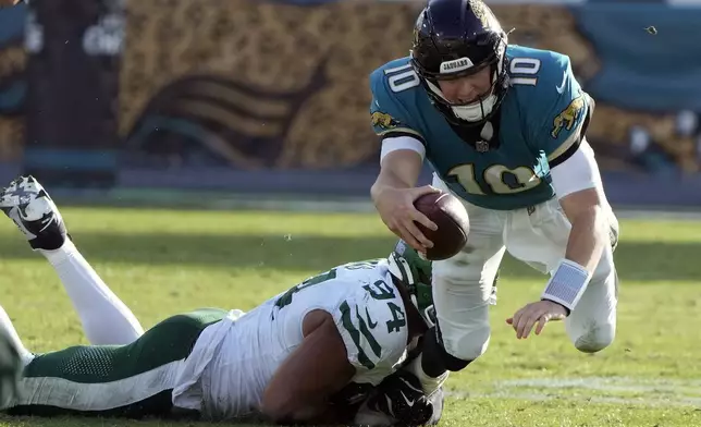 Jacksonville Jaguars quarterback Mac Jones (10) is tripped up by New York Jets defensive end Solomon Thomas (94) during the second half of an NFL football game Sunday, Dec. 15, 2024, in Jacksonville, Fla. (AP Photo/John Raoux)