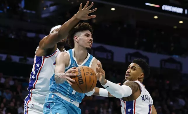 Charlotte Hornets guard LaMelo Ball, center, looks to pass the ball against Philadelphia 76ers forwards Guerschon Yabusele, left, and KJ Martin Jr., right, during the first half of an NBA basketball game in Charlotte, N.C., Monday, Dec. 16, 2024. (AP Photo/Nell Redmond)