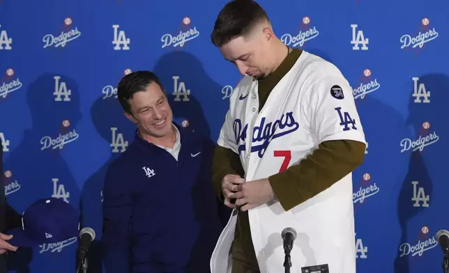 Los Angeles Dodgers pitcher Blake Snell, right, puts on his jersey as he is joined by president of baseball operations Andrew Friedman during a news conference Tuesday, Dec. 3, 2024, in Los Angeles. (AP Photo/Jae C. Hong)