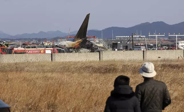 People watch as firefighters and rescue team members work at Muan International Airport in Muan, South Korea, Sunday, Dec. 29, 2024. (Cho Nam-soo/Yonhap via AP)