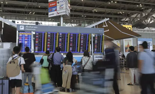 Tourists check an electronic board departure schedule at Suvarnabhumi International Airport in Samut Prakarn Province, Thailand, Sunday, Dec. 29, 2024. (AP Photo/Chatkla Samnaingjam)