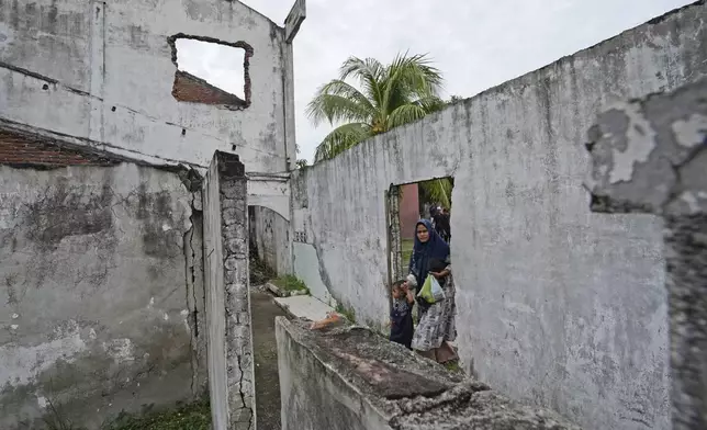 A woman walks trough an opening on the wall of a building badly damaged during the Indian Ocean tsunami in 2004 in Banda Aceh, Aceh province, Indonesia, Saturday, Dec 14, 2024. (AP Photo/Achmad Ibrahim)