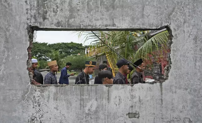 People are seen through a hole in the wall of a building damaged by 2004 Indian Ocean tsunami as they visit a giant barge housing a , a diesel power generator swept ashore by the killer wave, in Banda Aceh, Indonesia, Saturday, Dec 14, 2024. (AP Photo/Achmad Ibrahim)