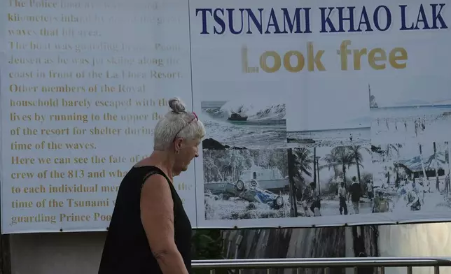 Tourist walk in from Tsunami Memorial poster at Khao Lak, Takuapa district of Phang Nga province, southern Thailand, Sunday, Dec. 8, 2024. (AP Photo/Sakchai Lalit)