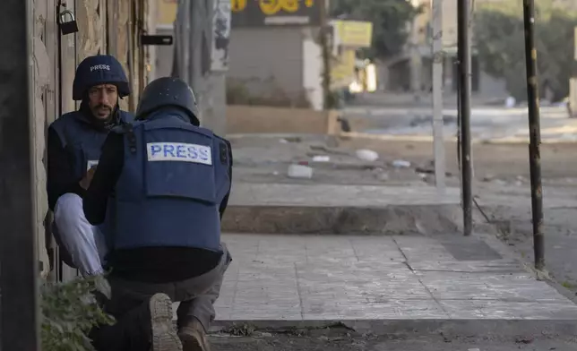 Journalists take cover from gunfire as Palestinian security forces mount a major raid against militants in the Jenin refugee camp in the Israeli-occupied West Bank, Monday, Dec. 23, 2024. (AP Photo/Majdi Mohammed)