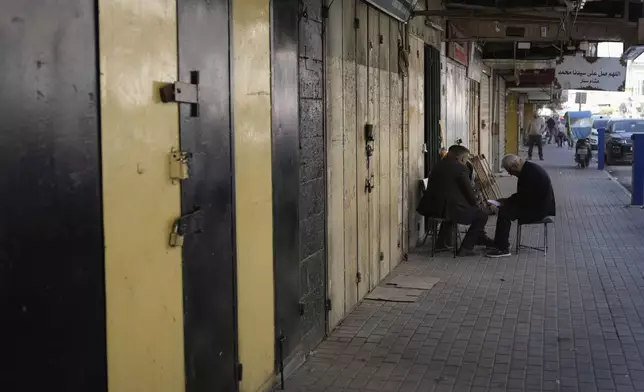 Palestinians sit in front of closed shops during a general strike called as Palestinian security forces mount a major raid against militants in the Jenin refugee camp in the Israeli-occupied West Bank, Monday, Dec. 23, 2024. (AP Photo/Majdi Mohammed)