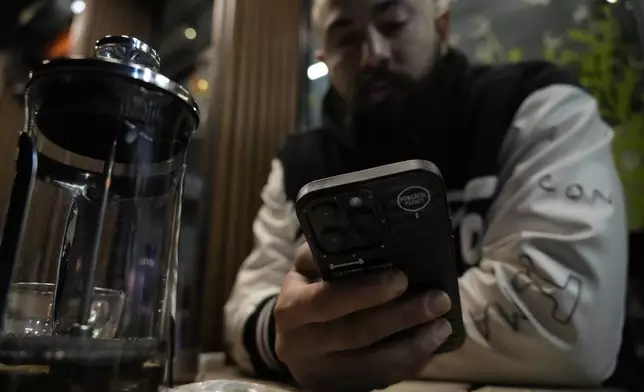 A man uses his smartphone as he sits in the alfresco dining area of a cafe in Tehran, Iran, Tuesday, Dec. 24, 2024. (AP Photo/Vahid Salemi)