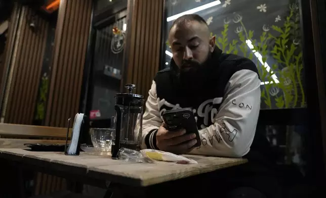 A man uses his smartphone as he sits in the alfresco dining area of a cafe in Tehran, Iran, Tuesday, Dec. 24, 2024. (AP Photo/Vahid Salemi)