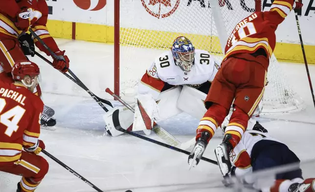 Florida Panthers' Dmitry Kulikov, bottom right, sends Calgary Flames' Jonathan Huberdeau, top right, flying as Panthers goalie Spencer Knight (30) looks on during second-period NHL hockey game action in Calgary, Alberta, Saturday, Dec. 14, 2024. (Jeff McIntosh/The Canadian Press via AP)