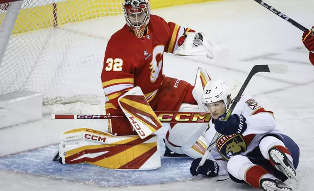 Florida Panthers' Eetu Luostarinen, right, crashes into Calgary Flames goalie Dustin Wolf, left, during second-period NHL hockey game action in Calgary, Alberta, Saturday, Dec. 14, 2024. (Jeff McIntosh/The Canadian Press via AP)