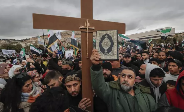 Syrians hold a copy of the Quran next to a Christian cross during a demonstration in support of unity among minorities and the ousting of the Bashar Assad government in Umayyad Square in Damascus, Syria, Friday, Dec. 27, 2024. (AP Photo/Omar Sanadiki)