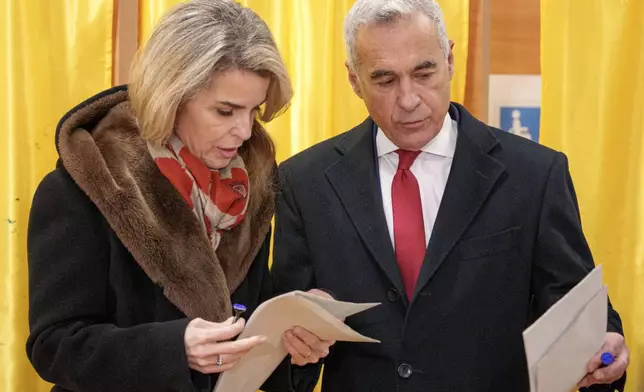 Calin Georgescu, an independent candidate for president who came first after the first round of presidential election, and his wife Cristela talk before casting their vote in the country's parliamentary election in Mogosoaia, Romania, Sunday, Dec. 1, 2024. (AP Photo/Andreea Alexandru)