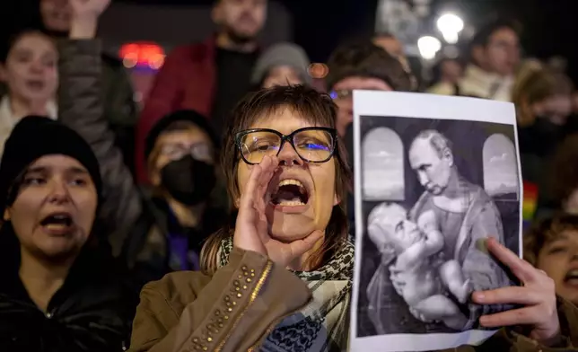 FILE - A woman shouts holding an altered version of a classic painting, depicting Russian President Vladimir Putin and Calin Georgescu, the independent candidate for Romanian presidency who won the first round of elections making it to the Dec. 8, runoff in Bucharest, Romania, Monday, Nov. 25, 2024. (AP Photo/Andreea Alexandru, File)