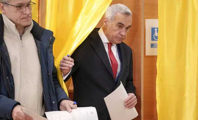 Calin Georgescu, right, an independent candidate for president who came first after the first round of presidential elections, exits a voting booth to cast his vote in the country's parliamentary election in Mogosoaia, Romania, Sunday, Dec. 1, 2024. (AP Photo/Andreea Alexandru)