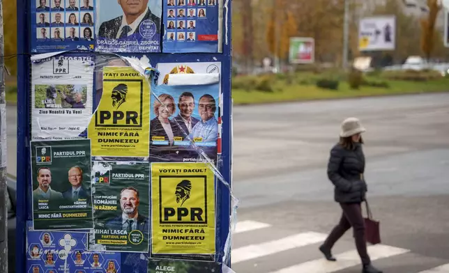 A woman walks by a panel displaying posters of various political parties, ahead of the country's Dec. 1 parliamentary elections, in Bucharest, Romania, Thursday, Nov. 28, 2024. (AP Photo/Andreea Alexandru)