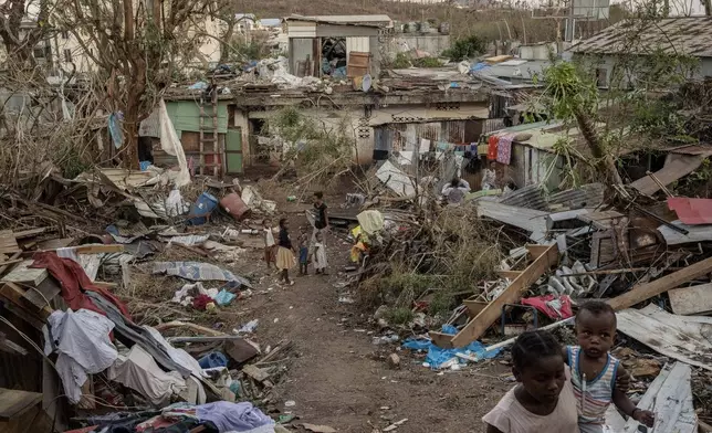 A family stands in the middle of wreaked houses in Mamoudzou, Mayotte, Thursday, Dec. 19, 2024 (AP Photo/Adrienne Surprenant)