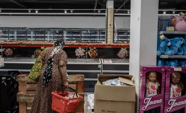 A woman looks at empty freezers as she looks for food supplies in Mamoudzou, Mayotte, Thursday, Dec. 19, 2024 (AP Photo/Adrienne Surprenant)