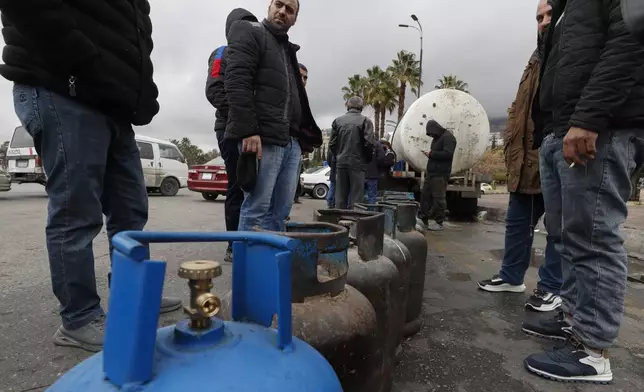 People stand next to propane cylinders as they wait in line to buy gas on a street at the Umayyad Square in Damascus, Syria, Saturday, Dec. 28, 2024. (AP Photo/Omar Sanadiki)