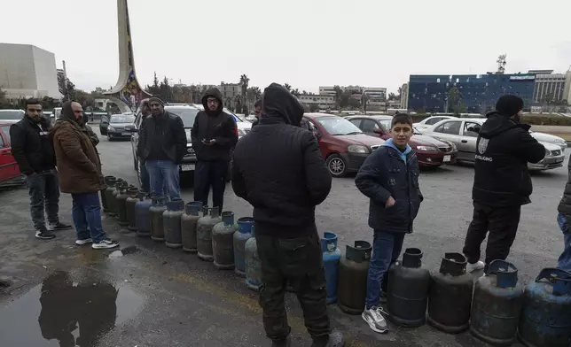 People stand next to cylinders as they wait in line to buy gas on a street at the Umayyad Square in Damascus, Syria, Saturday, Dec. 28, 2024. (AP Photo/Omar Sanadiki)