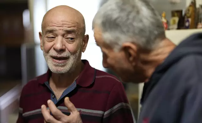 Suheil Hamwi, left, who spent 32 years in prison in Syria, reacts as a man shows him a picture of a missing Lebanese prisoner inside Syria, at Hamwi's home in Chekka, Lebanon, Tuesday, Dec. 10, 2024. (AP Photo/Hassan Ammar)